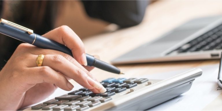 Hand using a calculator with a pen near a laptop, representing financial services, accounting, or IT support.