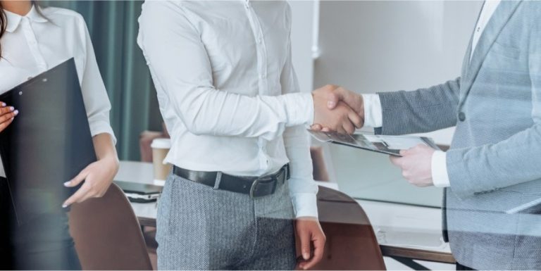 Two professionals shaking hands in an office, suggesting a business deal, partnership, or IT service agreement.